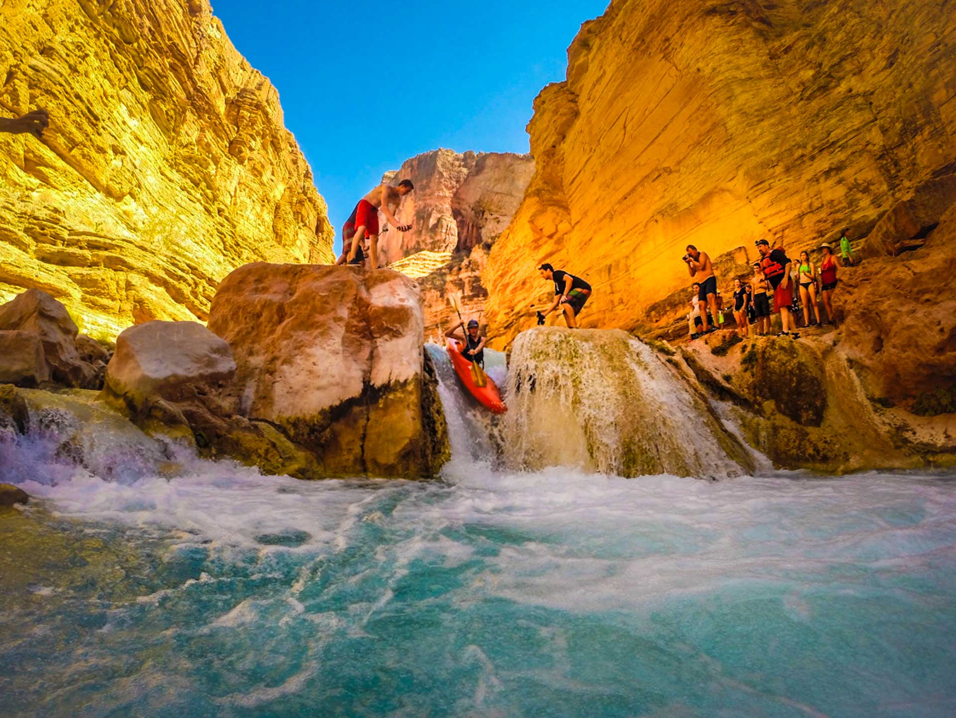 A group of people watching a man kayak during a whitewater rafting trip on the Colorado river in Grand Canyon National Park, Arizona.